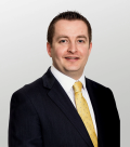 An image of James Kippling, MHA. He is looking at the camera wearing a black suit jacket with a white shirt and yellow tie.
